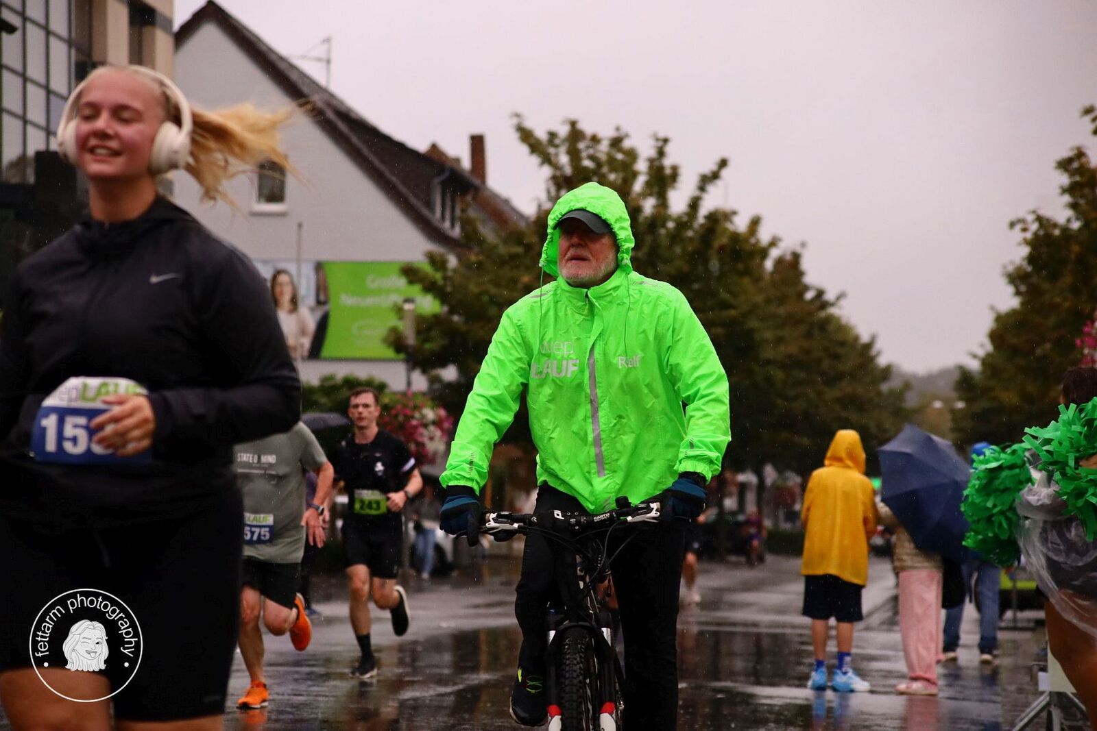 Läuferin mit Kopfhörern und das Führungsfahrrad in grüner wepLAUF-Jacke auf der regennassen Strecke