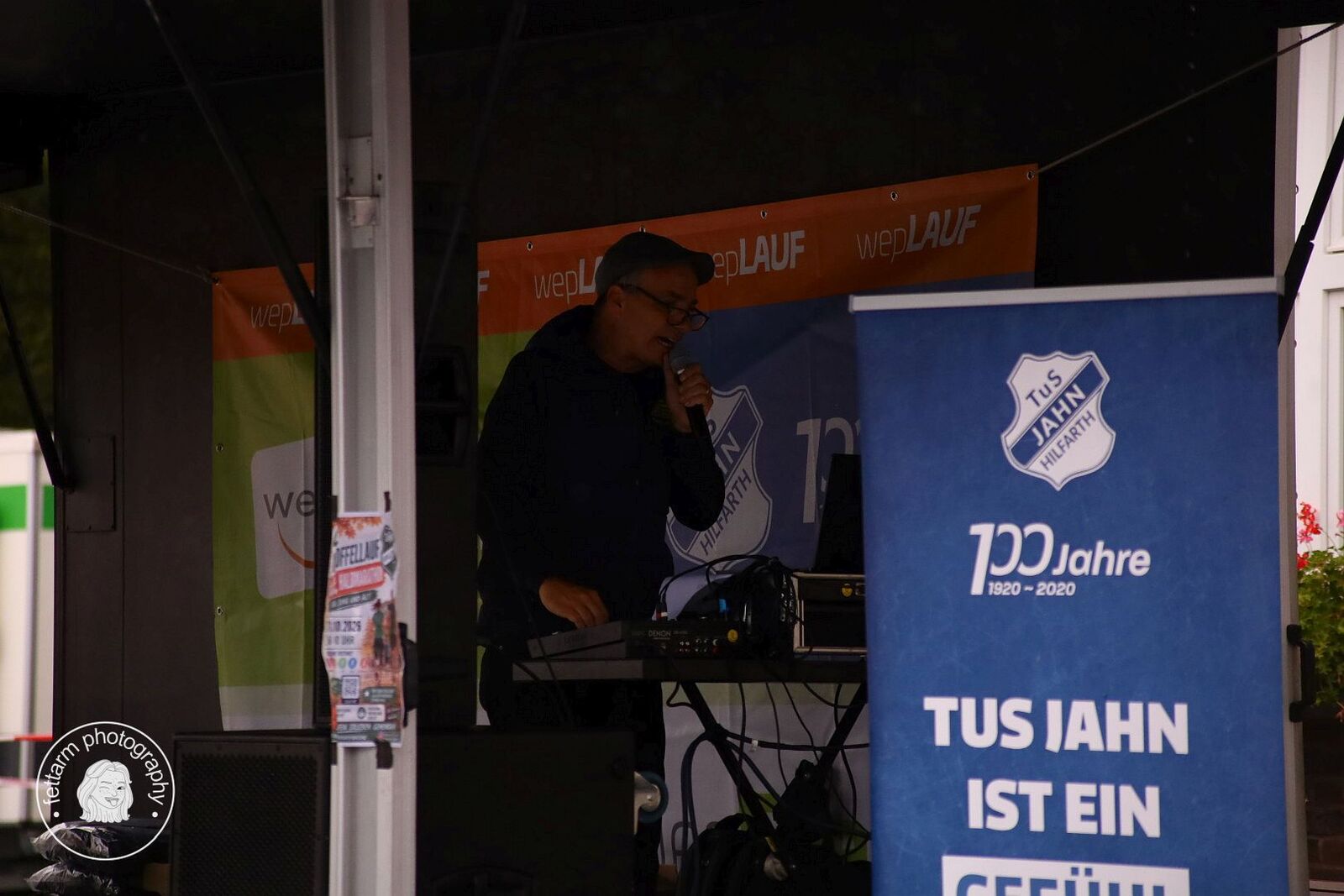 Der Moderator am Mikrofon auf der Bühne vor wepLAUF-Banner und TuS-Jahn-Roll-up