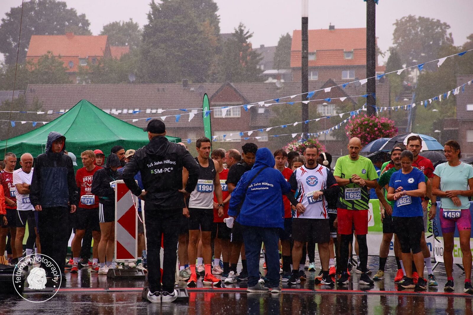 Läuferinnen und Läufer warten im Regen auf den Start, ein Helfer der TuS-Jahn-Leichtathletik gibt Anweisungen