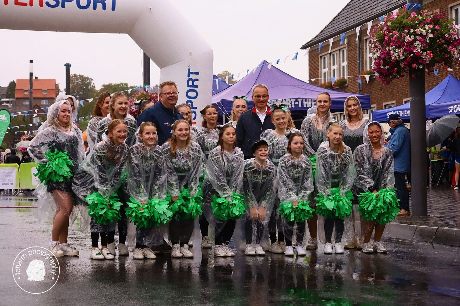 Gruppenfoto der Cheerleader in Regenponchos mit Vertretern von wep und TuS Jahn